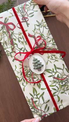 a person holding a wrapped present with a red ribbon and small tree decoration on it