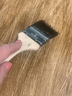 a hand holding a paint brush on top of a wooden table with white and black bristles