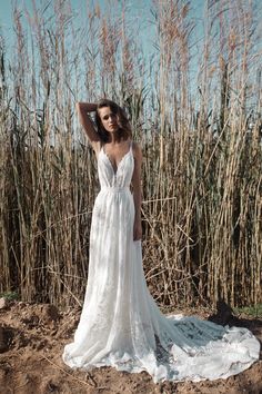 a woman in a white wedding dress standing on the ground next to tall reeds