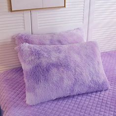 two purple pillows sitting on top of a bed next to a framed picture above them