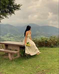 a woman in a dress sitting on a bench looking out over the valley and mountains