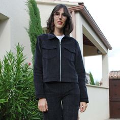 a woman standing in front of a house wearing black pants and a jacket with zippers