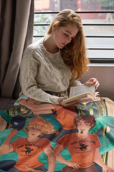 a woman reading a book on top of a bed in front of a large window