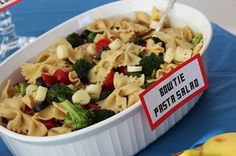 a white bowl filled with pasta and veggies on top of a blue table