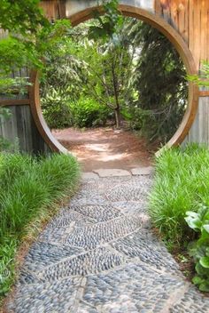 a stone path leading to a wooden gate with a circular mirror in the middle on it's side