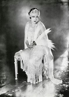 an old fashion photo of a woman sitting on a chair with feathers in her hair