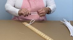 a woman in an apron is holding a ruler and threading it to a piece of wood