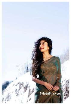 a woman standing in the snow wearing a green sari and looking off into the distance