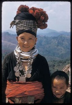 two young children standing next to each other on top of a hill with mountains in the background