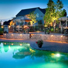 an outdoor swimming pool surrounded by landscaping and lights at night with patio furniture in the background