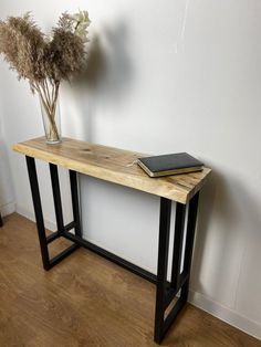 a wooden table topped with a book and a vase filled with flowers next to a wall