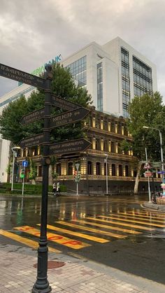 a street sign sitting on the side of a wet road next to a tall building