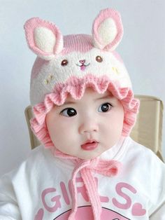 a small child wearing a pink hat with ears on it's head while sitting in a chair