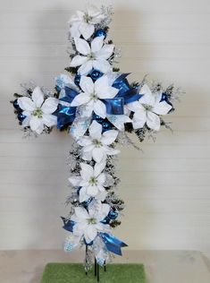 a cross made out of flowers and blue ribbon on a table with a white wall in the background