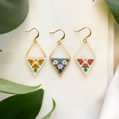 three pairs of beaded triangle earrings sitting on top of a table next to plants