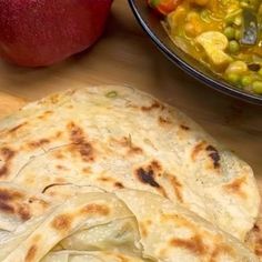 two pita breads sitting on top of a cutting board next to an apple