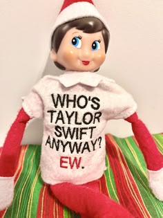 the elf is wearing a t - shirt that says who's taylor swift anyway?