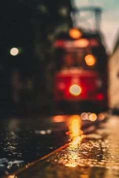 the back end of a red bus on a city street at night with lights reflecting off it's surface