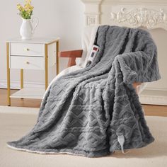 a gray blanket sitting on top of a chair next to a white dresser and lamp