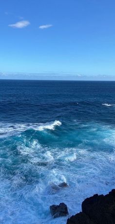 the ocean is blue and foamy with waves coming in from the rocks on the shore