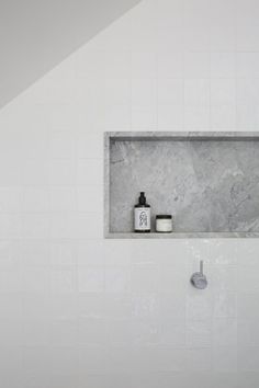 a white tiled bathroom with black and white accessories on the shelf above the shower head