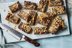 a cutting board topped with pieces of chocolate and nuts next to a knife on top of a table