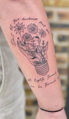 a person with a tattoo on their arm holding a potted plant and some flowers