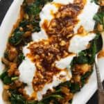 a white plate topped with spinach covered in yogurt and other toppings