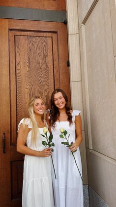 two beautiful young women standing next to each other in front of a door holding flowers