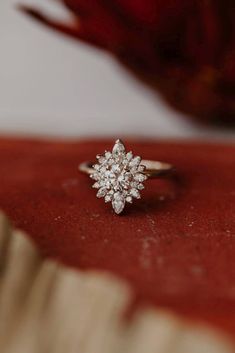 a diamond ring sitting on top of a red velvet covered table next to a flower