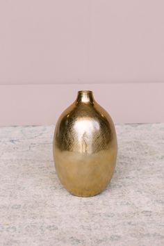 a gold colored vase sitting on top of a white countertop next to a pink wall