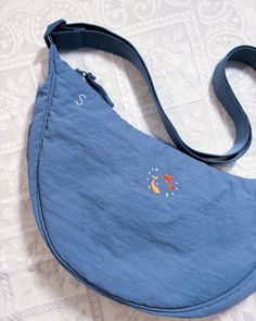 a blue purse with an orange fish embroidered on the front and shoulder strap, sitting on a white surface