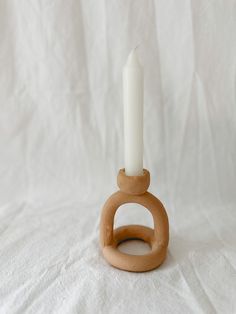 a wooden candle holder with a white candle in it on a plain cloth covered background