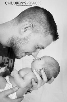 a man holding a baby and kissing it's face with his mouth open in black and white