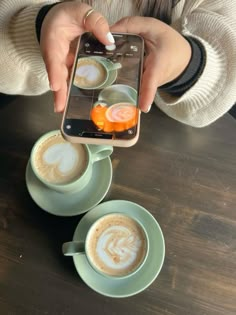 a person taking a photo of two cups of cappuccino and an orange slice