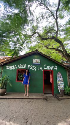 a woman standing in front of a green building with surfboards on the roof and door