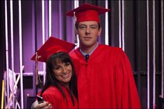 a man and woman in graduation gowns posing for a photo with their cell phone