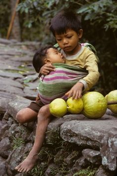 two young boys are sitting on some rocks and one boy is holding another child's head