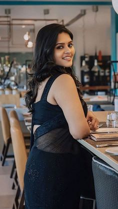 a woman in a black dress sitting at a table with wine glasses on the counter