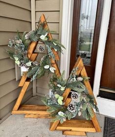 two wooden christmas trees with pine cones and greenery on them sitting in front of a door