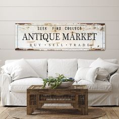 an antique market sign hangs on the wall above a white couch in a living room