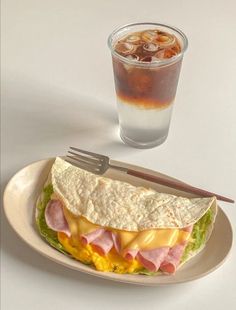 a sandwich with ham and cheese on it next to a glass of soda or cola