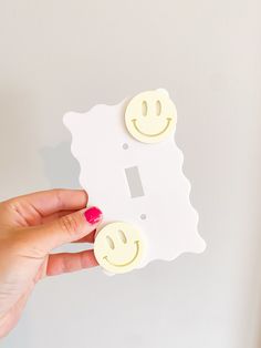 a person is holding two smiley faces in front of a light switch cover with one hand