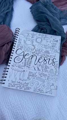 an open notebook sitting on top of a bed covered in sheets and scarves with the word genius written on it