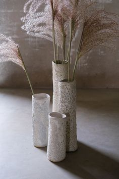 three white vases with flowers in them on a gray flooring area next to a wall