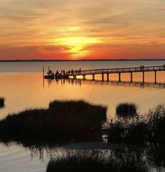 the sun is setting over some water and people are on a pier in the distance