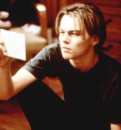 a young man sitting on the floor with his hand up to his face and looking at something