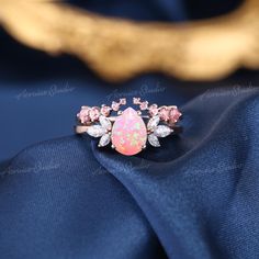 an opal and diamond ring sits on top of a blue satin material with gold accents