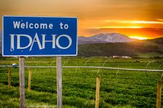 a welcome to idaho sign in the middle of a field with mountains in the background