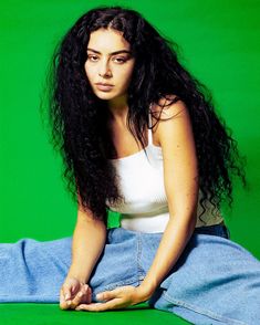 a woman with long black hair sitting on the ground in front of a green background